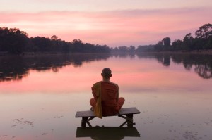 20 Jan 2011 --- Cambodia, Angkor Wat, Buddhist Monk sitting on platform over water in moat of temple complex, at sunset --- Image by © Martin Puddy/Corbis